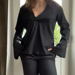 Svart blus från Gina Tricot - Snygg svart blus från Gina Tricot med v-ringning och långa ärmar. Perfekt för en stilren look. Blusen har en lös passform som ger en bekväm känsla. Passar bra till både jeans och kjol.