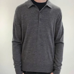 Grå tröja från Uniqlo - Säljer en stilren grå stickad tröja från Uniqlo. Tröjan har långa ärmar och en klassisk krage med knappar. Perfekt för en avslappnad men ändå elegant look. Tillverkad i ett mjukt material/ merinoull. Jag är 180 cm på bilden. Djurfrit hem 