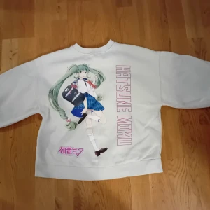 Grön sweatshirt med Hatsune Miku-tryck - Säljer en grön sweatshirt med ett stort tryck av Hatsune Miku på framsidan. Tröjan har långa ärmar och en rund halsringning. Perfekt för fans av Vocaloid och anime!