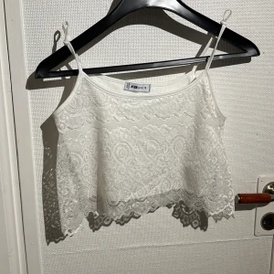 Vit spetslinne från FB Sister - Säljer en söt vit spetslinne från FB Sister. Den har tunna axelband och ett vackert spetsmönster som ger en romantisk känsla. Perfekt för varma sommardagar eller som ett lager under en kavaj.
