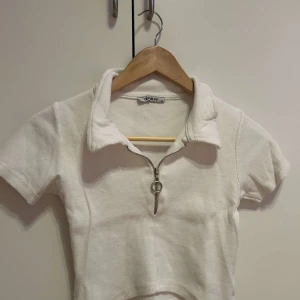 Vit ribbad polotopp  - Säljer en stilren vit ribbad polotopp.Toppen har korta ärmar och en dragkedja framtill som ger en cool detalj. Perfekt för en avslappnad look.