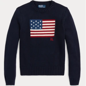 Mörkblå stickad tröja från Polo Ralph Lauren - Säljer en mörkblå stickad tröja från Polo Ralph Lauren med en stor amerikansk flagga på framsidan. Tröjan har långa ärmar och ribbstickade muddar vid ärmslut och nederkant. Perfekt för en stilren och avslappnad look.