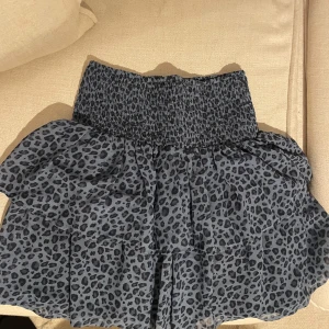 Blå leopardmönstrad kjol - Säljer en superfin blå leopardmönstrad kjol med smockdetaljer i midjan. Kjolen är kort och har en luftig passform, perfekt för sommardagar eller en festkväll. Materialet känns lätt och bekvämt. Passar perfekt med en enkel topp eller stickad tröja. 🐆💙