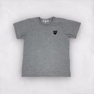 CDG T shirt - Säljer en snygg grå t-shirt från PLAY med ett coolt svart hjärta med ögon på bröstet. Den är i nytt skick och har en normal passform. Perfekt för vardagsbruk eller att styla upp med en jacka. Materialet känns mjukt och skönt mot huden. Har en pytte liten hål bakom som inte märks alls. 