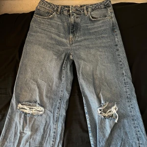 Blå jeans med slitningar - Säljer ett par blå jeans i vintage-stil med coola slitningar på knäna. De har en klassisk femficksdesign och en bekväm passform. Perfekta för en avslappnad look! 🕶️