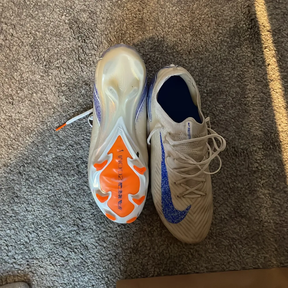 Säljer ett par Nike Gripknit fotbollsskor i beige med blå detaljer och den låga strumpan. Skorna har en cool design med snörning och en sula i orange och blått för extra grepp på planen. Perfekta för fotbollsspelare som vill ha både stil och funktionalitet. Nypris ca 3500kr. Priset kan diskuteras vid snabb affär.. Skor.