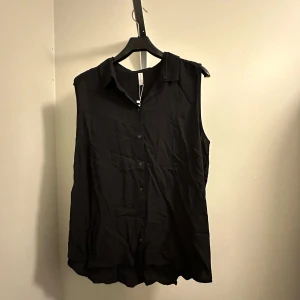 Svart blus - Svart ärmlös blus med knappar framtill. Perfekt för både vardag och festliga tillfällen. Prislappen är kvar från New Yorker i storlek XXL!