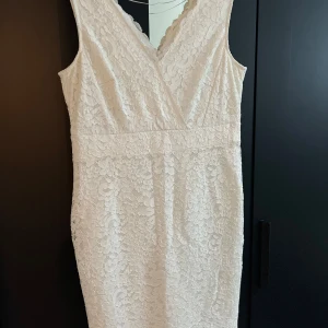 Vit spetsklänning från Esprit - Säljer en elegant vit spetsklänning från Esprit. Klänningen har en v-ringad design och är ärmlös, perfekt för sommarens fester. Den har en omlott-look framtill och är i ett vackert spetsmaterial som ger en romantisk känsla. Passar perfekt för både bröllop och andra festliga tillfällen.