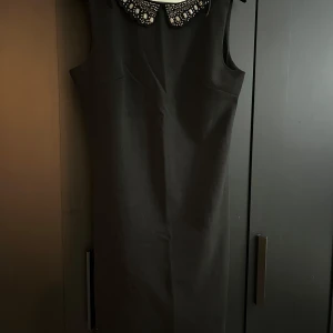 Svart klänning från Lulumary - Elegant svart klänning köpte i Frankrike från Lulumary i storlek L. Den är ärmlös och har en vacker pärlbroderad krage som ger en lyxig touch. Perfekt för festliga tillfällen eller en utekväll. Klänningen är i nyskick och har en figurnära passform.