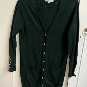 Svart kofta från First Class - Säljer en elegant svart kofta från First Class i storlek M. Den har långa ärmar med snygga knappar vid ärmsluten och en knappslå framtill. Perfekt för både vardag och fest! 🖤