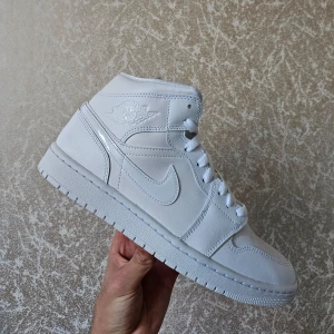 Nike Air Jordan 1 Mid Vit - Nike Air Jordan 1 Mid i vit färg. Snygga och stilrena skor som passar till många olika tillfällen.