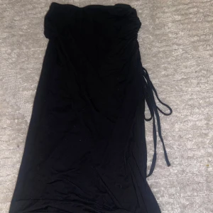 Svart kjol med knytband - Snygg svart kjol med knytband i midjan och slits som man kan välja vart den ska vara beroende på hur man spänner banden. Perfekt för både vardag och fest! Kjolen har en enkel design som gör den lätt att matcha med olika toppar och accessoarer. Ett måste i garderoben för alla som älskar stilrena plagg.