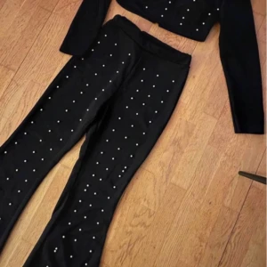 Svart croppad topp med pärlor - Snygg svart croppad topp med långa ärmar och pärldetaljer. Perfekt för en festlig kväll eller en utekväll med vänner. Toppen är både stilren och trendig, vilket gör den lätt att matcha med olika outfits.