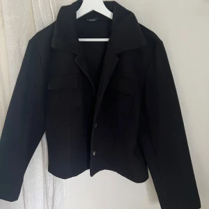 Svart jacka från Boohoo - Snygg svart jacka från Boohoo. Den har en liten krage och knappar framtill. Perfekt för höst och vår, med en stilren look som passar till allt. Jackan har långa ärmar och två fickor framtill. Lite nopprig men inget som syns mycket!