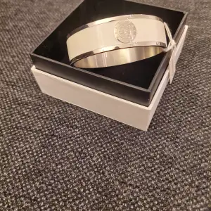 Snyggt och stilrent armband i silver och vit från Dyrberg/Kern. Armbandet har en elegant design med en rund logodetalj i mitten. Perfekt för att ge en touch av lyx till vilken outfit som helst. Kommer i originalförpackning.