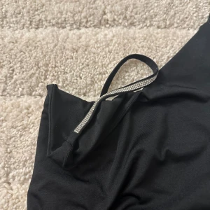 Svart linne, med silver detaljer. - Helt oanvänd, man knäpper den som en body. Kan användas på fest eller till vardags.