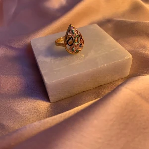Färgglad mandelformad ring - Säljer en unik och färgglad ring med en droppformad design. Ringen har ett vackert mönster med olika färger som blått, grönt och orange. Perfekt för att ge en färgklick till din outfit. Passar både till vardags och festliga tillfällen.