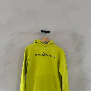 Gul hoodie från Sail Racing - Säljer en cool gul hoodie från Sail Racing. Den har en stor logga på bröstet och en praktisk magficka. Perfekt för både vardag och chill. Passar bra till jeans eller träningsbyxor. Grym färg som verkligen sticker ut!