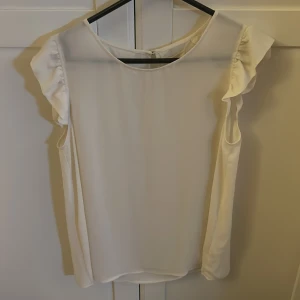 Vit blus från Holly & White - Säljer en elegant vit blus från Holly & White i storlek 40. Blusen har korta ärmar med volangdetaljer och en rund halsringning. Perfekt för både vardag och festliga tillfällen. Den är i mycket bra skick och redo för en ny garderob! ✨