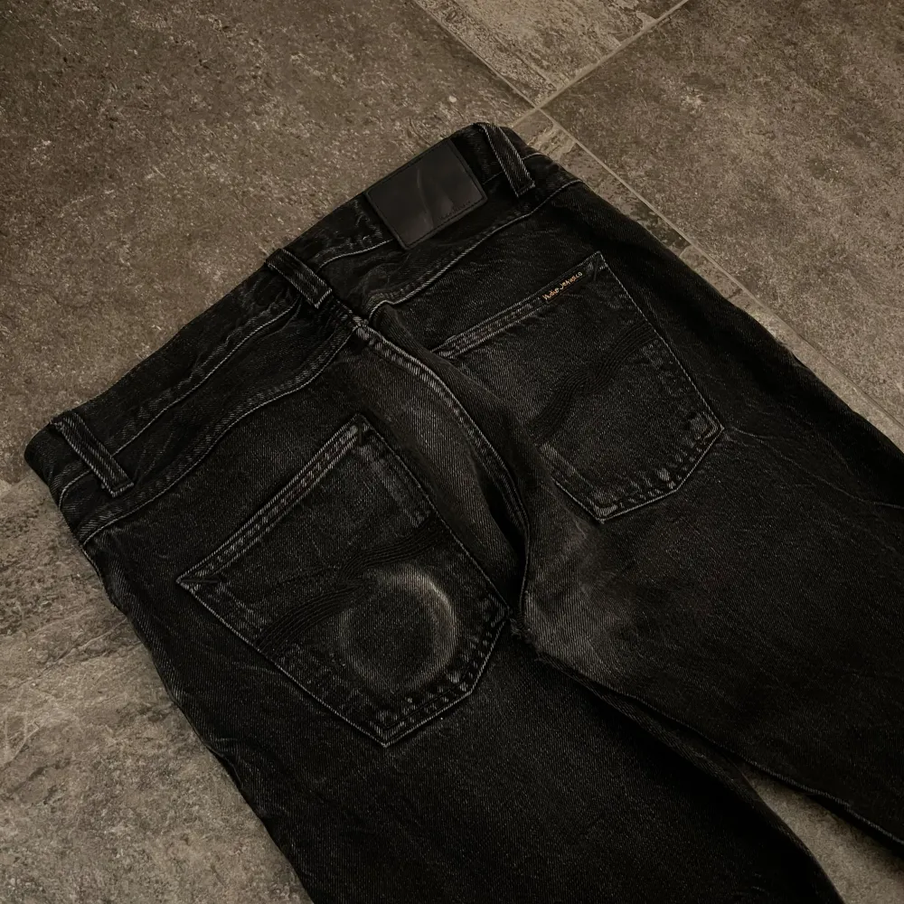 Säljer ett par svarta jeans från Nudie Jeans i storlek 32/34. De är tillverkade av 100% ekologisk bomull och har en klassisk femficksdesign. Jeansen har en straight passform och är i bra skick med lite slitage för en cool look. Perfekta för både vardag och fest!. Jeans & Byxor.