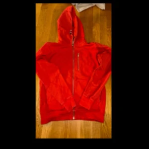 Röd sailracing hoodie  med dragkedja - Säljer en snygg röd sailracing hoodie med dragkedja framtill och en praktisk bröstficka. Perfekt för kyliga dagar och har en skön huva. Jackan är i bra skick och redo för nya äventyr! 🔥