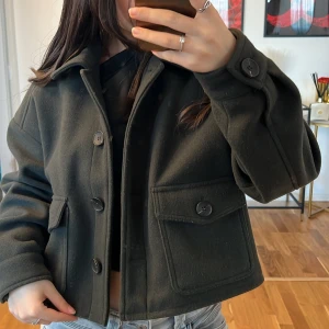 Mörkgrön kort kappa från Zara  - Säljer en snygg mörkgrön kappa från Zara med stora knappar framtill. Den har en kortare passform och två stora fickor med knappar. Perfekt för höst och vår, och funkar både till vardags och fest. Jackan är i mycket bra skick och har långa ärmar💓