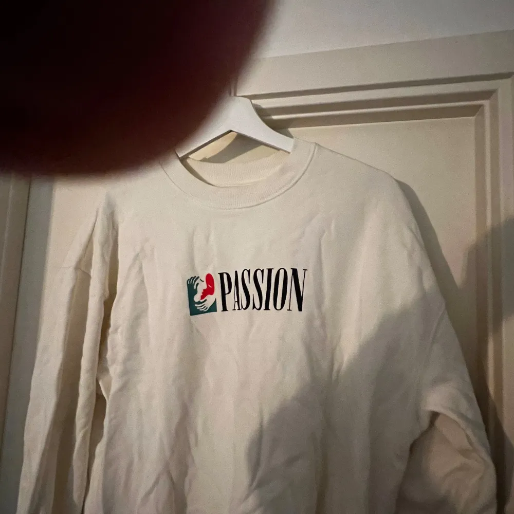 Säljer en snygg vit sweatshirt  i storlek M. Tröjan har ett coolt tryck med texten 'PASSION' och en design i rött och grönt. Perfekt för en avslappnad stil eller att bära till vardags. Den är i bra skick och superbekväm! Kan mötas upp i Karlstad . Tröjor & Koftor.