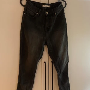 Svarta jeans med fransade kanter - Säljer ett par svart/grå jeans från NAKD. De har en fransad kant vid bensluten, klassisk design med en rak passform och slutar ovanför ankeln. Jeansen är i bra skick och passar till de flesta outfits!