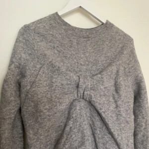 Stickad tröja  - Stickad tröja av ylle från COS med en rosett på ryggen, har ett jättelitet hål på underarmen 