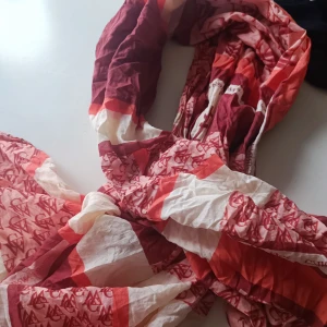 Röd och vit halsduk med mönster - Säljer en snygg och färgglad halsduk i rött och vitt. Den har ett coolt mönster som ger den en unik stil. Perfekt för att liva upp din outfit under höst och vår. Materialet känns lätt och luftigt, vilket gör den bekväm att bära.