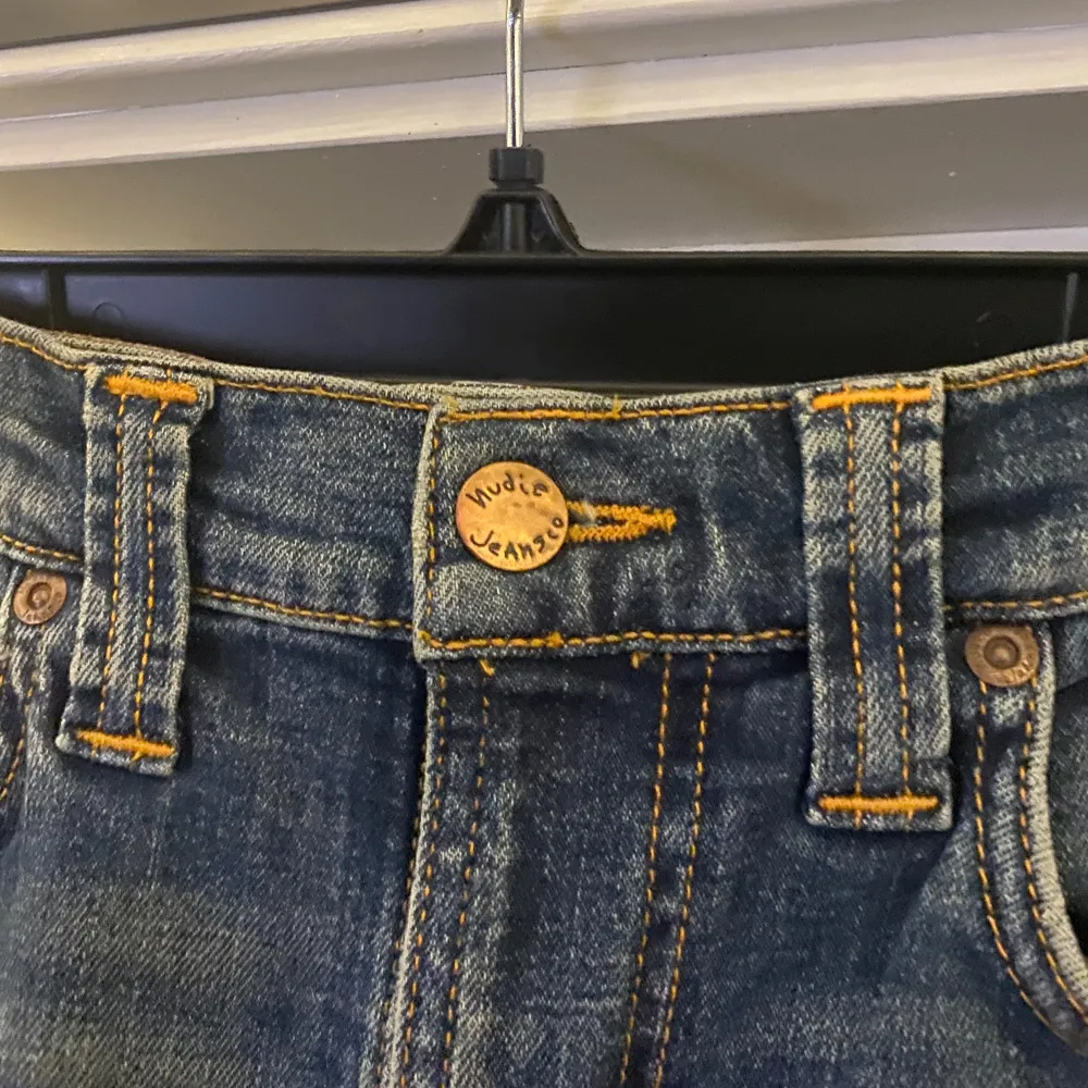 Säljer ett par snygga jeans från Nudie Jeans. De är i en klassisk blå färg med snygga slitningar och kontrastsömmar i orange. Perfekta för en casual look och passar till det mesta. De har en knappgylf och fem fickor. Det är skinny jeans . Jeans & Byxor.