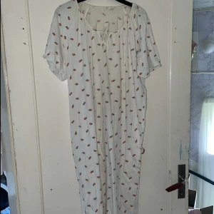 Vit blommig klänning - Säljer en söt vit klänning med små blommor i rött och grönt. Klänningen har korta ärmar och en bekväm passform med knytning vid halsen. Perfekt för sommarens alla tillfällen!