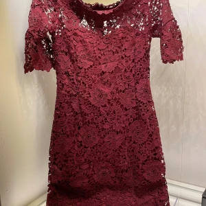 Vinröd spetsklänning - Säljer en superfin vinröd spetsklänning med kortärmad design. Klänningen har ett vackert blommigt mönster och en dragkedja i ryggen. Perfekt för festliga tillfällen! Bra skick, inga defekter.
