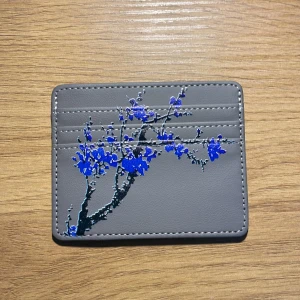 Grisch plånbok  - Säljer en stilren grå plånbok med ett vackert blått blommönster på framsidan. Plånboken har flera kortfack och är perfekt för att hålla ordning på dina kort. Den är kompakt och lätt att bära med sig.