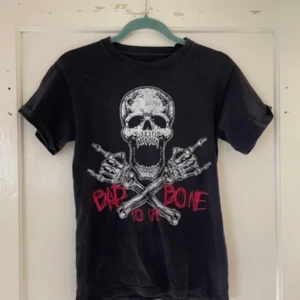Svart t-shirt med dödskalletryck från EMP - Säljer en svart t-shirt från EMP med ett coolt dödskalletryck och texten 'Bad to the Bone' i rött. Perfekt för en rockig stil! T-shirten är i storlek S och har korta ärmar.
