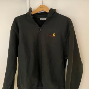 Mörkgrön zip från Carhartt - Säljer en grön  tröja från Carhartt med dragkedja och broderad logga på bröstet. Perfekt för en casual look och passar till det mesta. Tröjan har långa ärmar och är i mycket bra skick. Perfekt för höst och vinter!