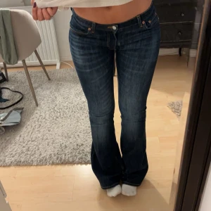 Mörkblå bootcut jeans lågmidjade - Säljer ett par snygga mörkblå bootcut jeans i mycket bra skick. De är lågmidjade och har en klassisk femficksdesign med knappar och dragkedja. Perfekta för både vardag och fest, jag är 170 lång, de är använda typ 1 gång
