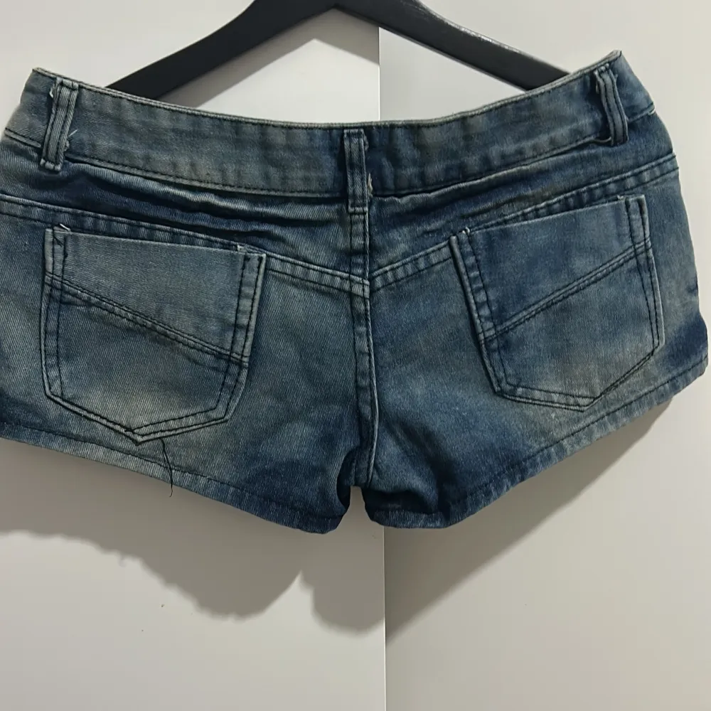 Snygga blå jeansshorts i storlek XL med coola knapplås och glittriga detaljer framtill. Perfekta för sommardagar eller en avslappnad fest. De har en låg midja och klassiska bakfickor. Passar perfekt till en t-shirt eller linne för en avslappnad look.. Shorts.