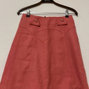 Rosa kjol från H&M - Säljer en superfin rosa kjol från H&M i storlek 34. Kjolen har en snygg A-linjeform och dekorativa knappar framtill. Perfekt för både vardag och fest! Den är i mycket bra skick och har en dragkedja bak för enkel påklädning.