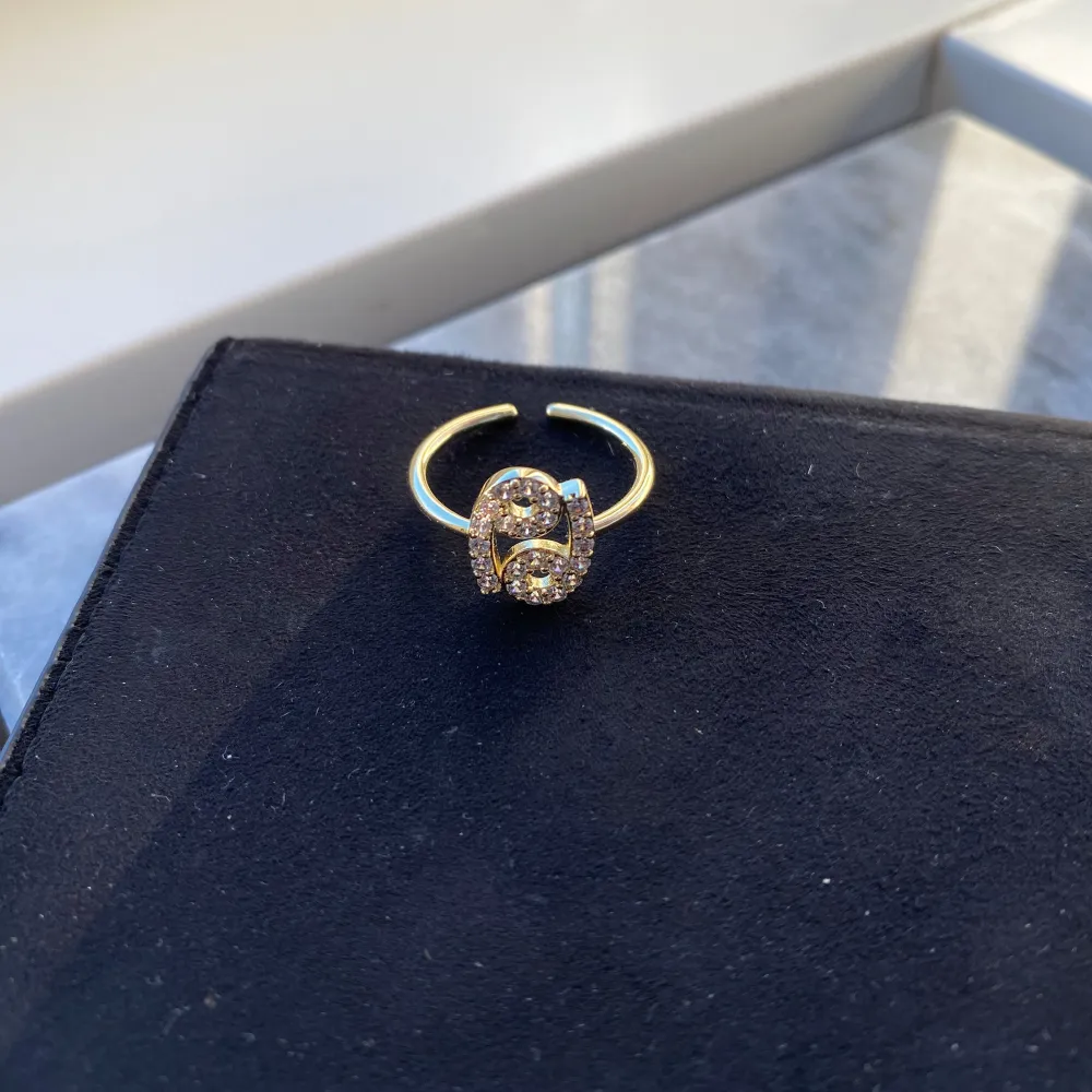 IOAKU Zodiac Sparkle Ring i kräftans stjärntecken.   Ringstorlek: En storlek, justerbar      Ringen är gjord av mässing och är fri från nickel, bly och kadmium. Ringdesignen är pläterad i 5 lager med högkvalitativ 18K guld och miljövänlig produktion.                                           Använd vid ett tillfälle och är i nyckick.  Nypris 349 kr. . Accessoarer.