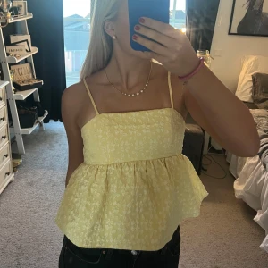 Gul blommig topp - Säljer en söt gul topp med blommigt mönster. Den har smala axelband och en luftig passform med volangdetalj. Perfekt för sommardagar! 🌼 hör av er om fler bilder💕 