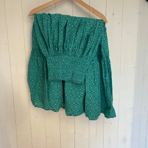 Turkos lång kjol  - Säljer en superfin grön klänning med ett unikt mönster. Den har en smockad överdel som ger en bekväm passform och vida ärmar. Perfekt för både vardag och festliga tillfällen. Klänningen är i mycket bra skick och passar perfekt till vår och sommar.