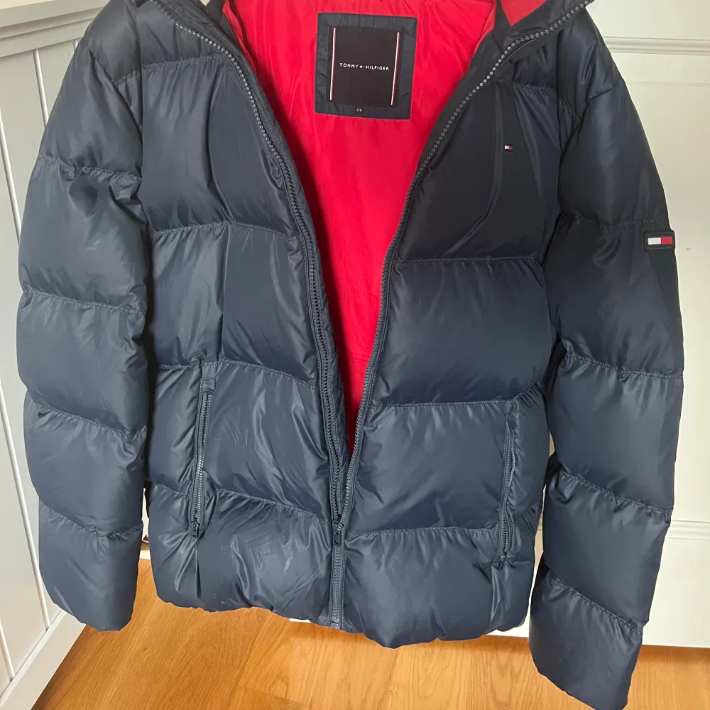 Säljer en snygg blå dunjacka från Tommy Hilfiger i storlek 176. Jackan har en cool röd insida och en praktisk huva. Perfekt för kalla vinterdagar med sin varma och puffiga design. Den har en dragkedja framtill och är i mycket bra skick. Passar både till vardags och lite finare tillfällen.. Jackor.