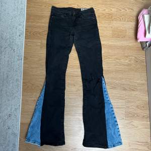 Säljer ett par unika bootcut jeans med en cool mix av svart och blå denim. De har en sliten detalj på ena benet som ger en edgy look. Perfekta för att sticka ut i mängden! Passar både till vardags och fest. 🖤💙