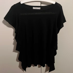 Svart topp från Zara - Snygg svart topp från Zara i storlek M. Den har en lös passform och korta ärmar, perfekt för både vardag och fest. Materialet känns mjukt och bekvämt mot huden. Ett stilrent plagg som passar till det mesta!