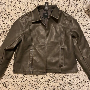 Svart skinnjacka från Boohoo - Säljer en snygg svart skinnjacka från Boohoo i mycket bra skick. Jackan har en dragkedja framtill och två fickor. Perfekt för höst och vår, med en stilren look som passar till det mesta. Jackan har långa ärmar och en klassisk krage.