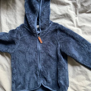 Blå teddyjacka från H&M - Mysig blå teddyjacka från H&M i herrstorlek S. Perfekt för kyliga dagar med sin mjuka och fluffiga textur. Jackan har en dragkedja framtill och en praktisk huva. Den är i mycket bra skick och redo för nya äventyr!