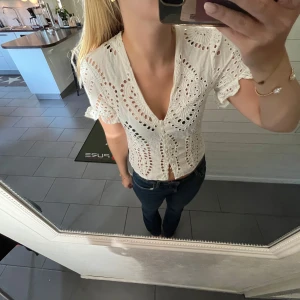 Vit blus med spetsdetaljer - Säljer en superfin vit blus med spetsdetaljer och korta ärmar. Den har en v-ringad design och knappar framtill. Perfekt för sommardagar eller en avslappnad vårlook. Blusen är i mycket bra skick och ger en romantisk touch till vilken outfit som helst.