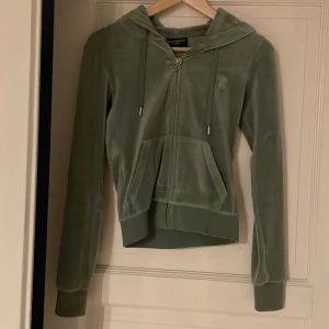 Grön hoodie från Juicy Couture - Säljer en supermjuk och snygg grön hoodie från Juicy Couture i storlek XXS. Perfekt för en avslappnad stil eller mysiga dagar hemma.💗💗💗 köpt för 1200kr 💗 färgen heter chinos green 💗💗 jag har även byxorna till i samma färg och storlek så kontakta om frågor eller om fler bilder 💗