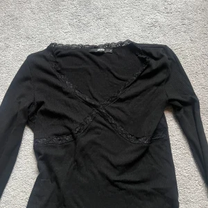 Svart ribbad topp från Bik Bok - Säljer en snygg svart ribbad topp från Bik Bok i storlek S. Toppen har långa ärmar och fina spetsdetaljer vid halsringningen och över bysten. Perfekt för både vardag och fest! 🖤